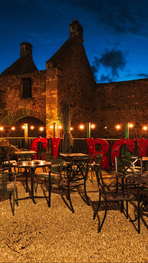Outdoor seating area with tables and chairs in front of a stone building at night.
