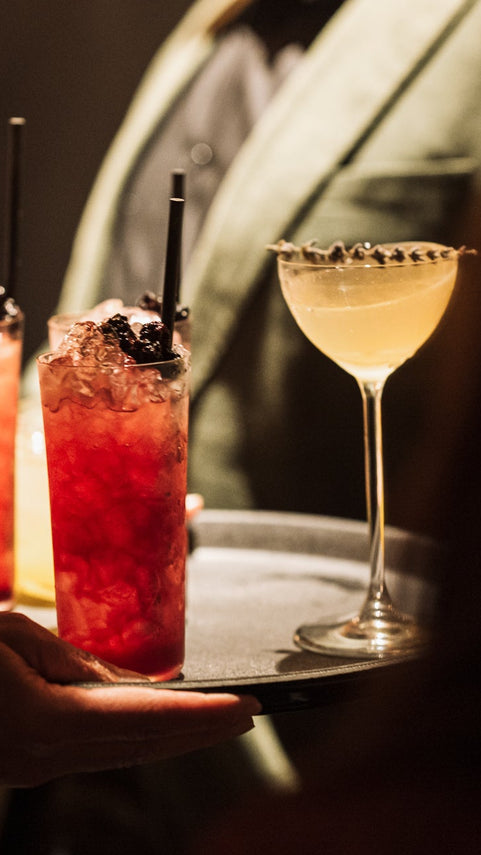 Tray of cocktails with a focus on a red cocktail and a wine glass.